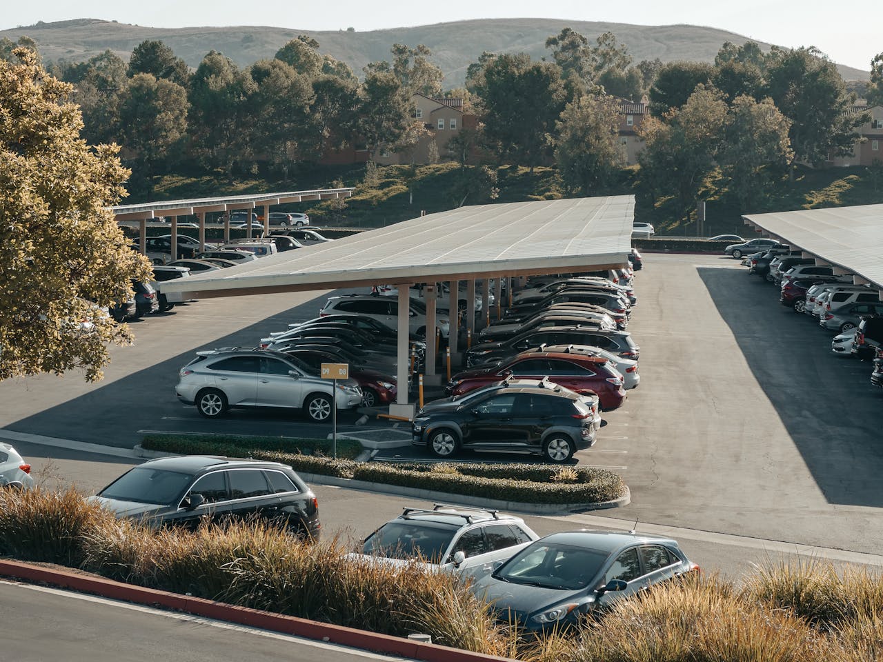 View of a large parking lot with solar panel shades and diverse vehicles parked.